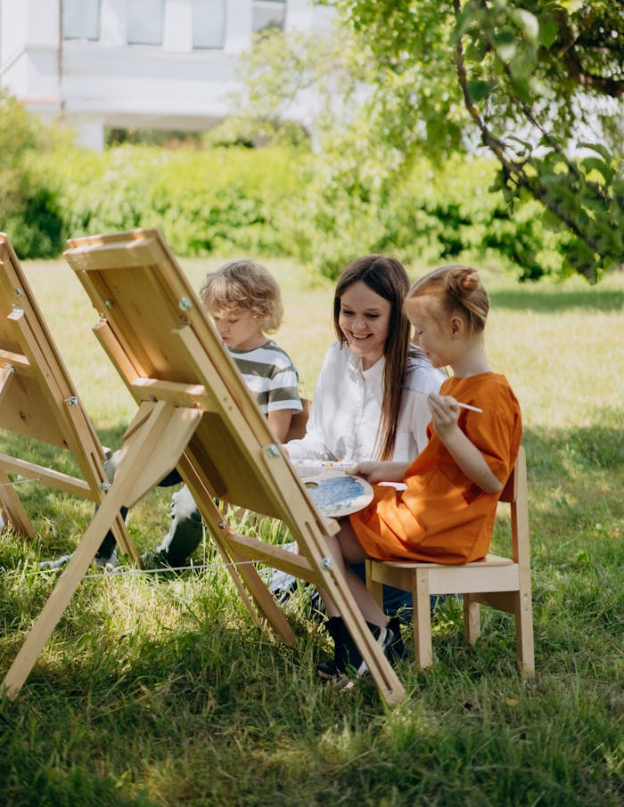 Home Children and teacher painting outdoors, enjoying a creative lesson under a tree.